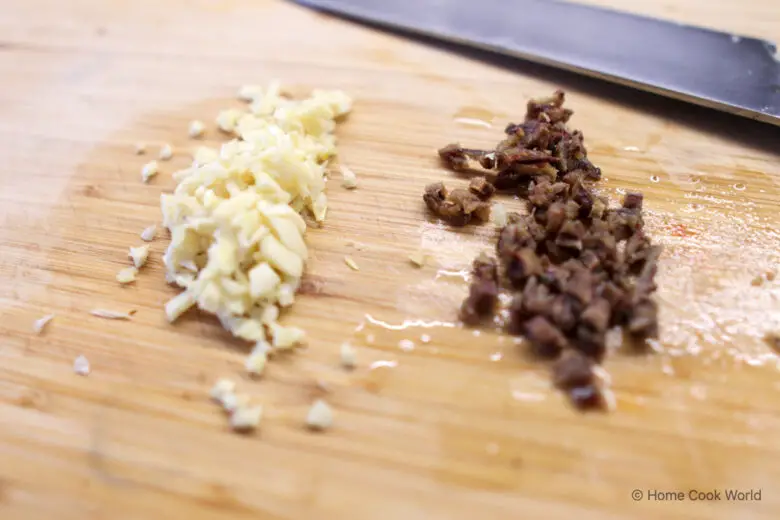 Minced garlic and minced anchovy on a wooden cutting board